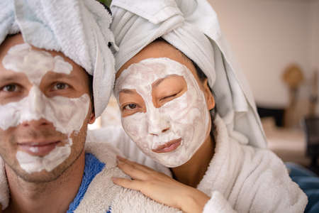 Husband and wife are lying on couch home and doing restoring face masks portrait. Healthy facial skin care at home help conceptの写真素材