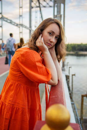 portrait of white caucasian woman with red hair and blue eyes in an orange dress stands on the...
