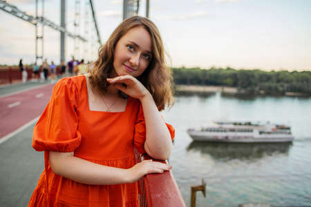 portrait of white caucasian woman with red hair and blue eyes in an orange dress stands on the...
