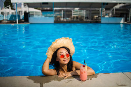 Portrait beautiful young asian woman with cocktail relax smile around outdoor swimming pool in hotel resortの写真素材