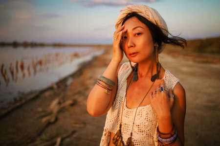 Photo of beautiful boho styled model wearing white and silver bohemian jewelery on the beach in...