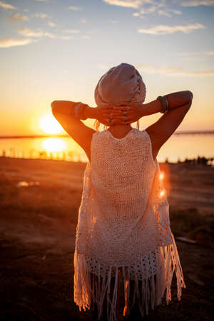 Photo of beautiful boho styled model wearing white and silver bohemian jewelery on the beach in sunsetの写真素材