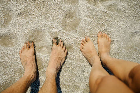 Pink Salt deposits on shores of beautiful pink lake. Foot of couple standing on sea salt beach.の写真素材