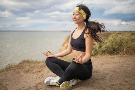 Beautiful slim asian woman doing yoga on a cliff, behind an amazing view near sea.