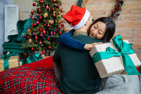 Beautiful young couple celebrating at home. handsome man is giving his asian girlfriend a gift boxの写真素材