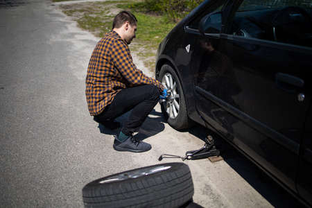 Auto mechanic man with electric screwdriver changing tire outside. Car service. Hands replace tires on wheels. Tire installation concept.の写真素材
