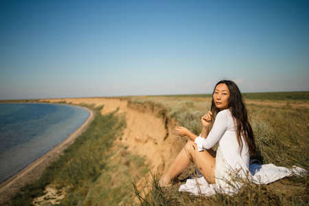 Asian girl sitting on a rock overlooking the ocean in silenceの写真素材