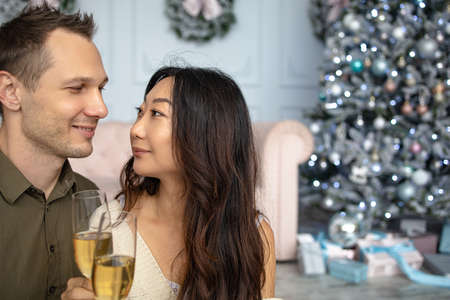Christmas mixed race couple cheers together near ornate festive Eve. Holidays celebrations family togetherの写真素材