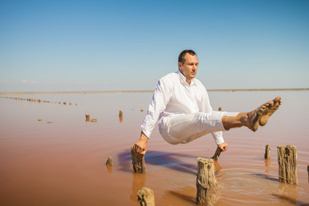 Fit young man practicing sun greeting yoga on the beach of pink lake at sunsetの写真素材