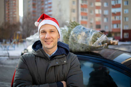 A man in Santa Claus hat tying a Christmas tree to the roof of the car to bring it homeの写真素材