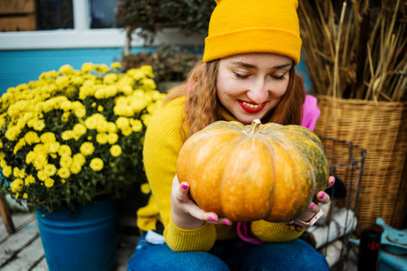 Close up, Beautiful young blond woman holding orange pumpkin in garden.の写真素材