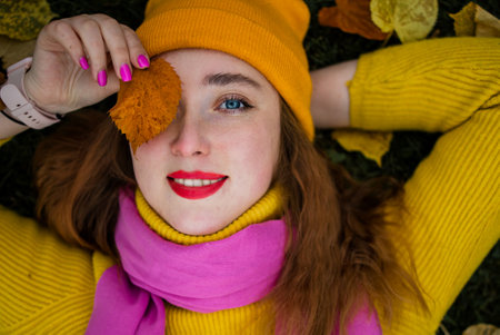 Cute red hair woman in yellow sweater holding autumn leaves in nature.の写真素材