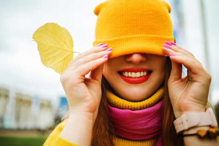 Cute red hair woman in yellow sweater holding autumn leaves in nature.の写真素材