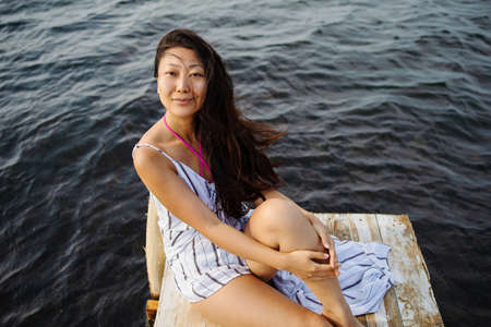 Beautiful asian woman sitting alone lonely on wooden bridge looking at outdoor ocean.の写真素材