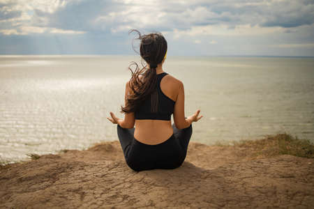 Beautiful asian woman doing yoga on a cliff, behind an amazing view near sea.の写真素材
