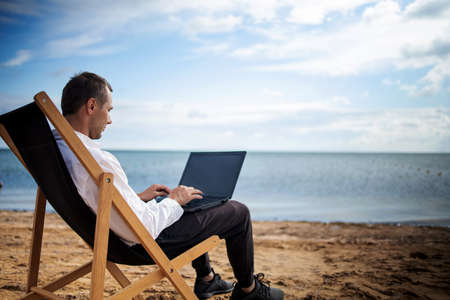 Young man with tablet computer during tropical beach vacation. Freelancer working on laptop lying on sun lounger.の写真素材