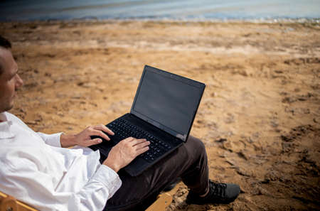 Young man with tablet computer during tropical beach vacation. Freelancer working on laptop lying on sun lounger.の写真素材