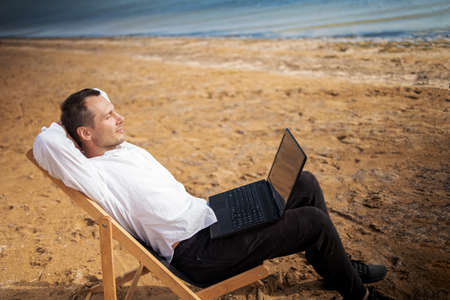 Young man with tablet computer during tropical beach vacation. Freelancer working on laptop lying on sun lounger.の写真素材