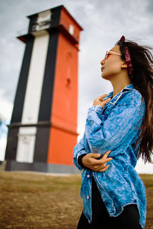 Asian woman sightseeing lighthouse seascape in europe travel outdoor recreation lifestyle concept. girl hair in the wind wearing a denim jacketの写真素材