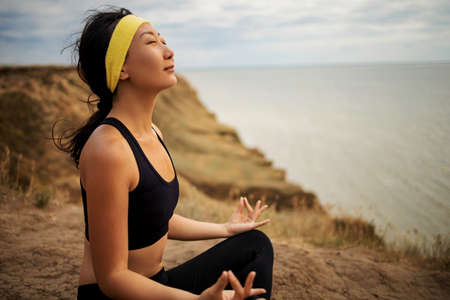 Beautiful asian woman doing yoga on a cliff, behind an amazing view near sea.の写真素材