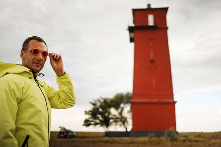 Young handsome man sightseeing lighthouse seascape in travel outdoor recreation lifestyle concept. Man in the wind wearing yellow raincoatの写真素材