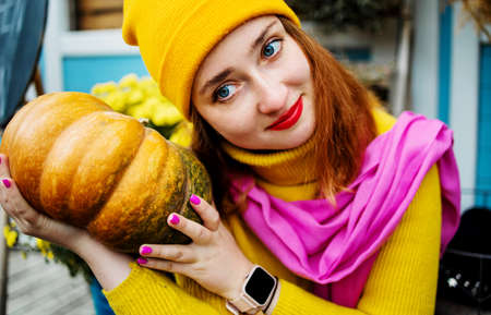 Close up, Beautiful young blond woman holding orange pumpkin in garden.の写真素材