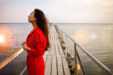 Beautiful asian woman wearing red suit sitting on old wooden pierの写真素材