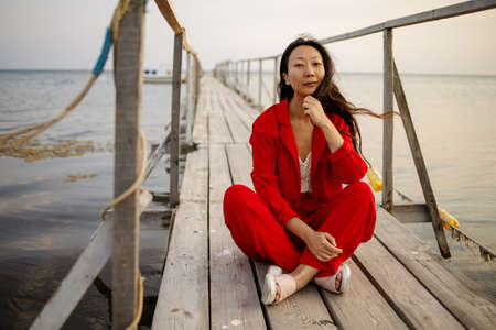 Beautiful asian woman wearing red suit sitting on old wooden pierの写真素材