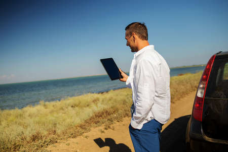 young caucasian businessman near a car working on a tablet, communicates on a video call.の写真素材