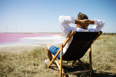 Businessman sitting in deck chair at beach of pink sea on sunny day.の写真素材