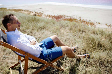 Businessman sitting in deck chair at beach of pink sea on sunny day.の写真素材