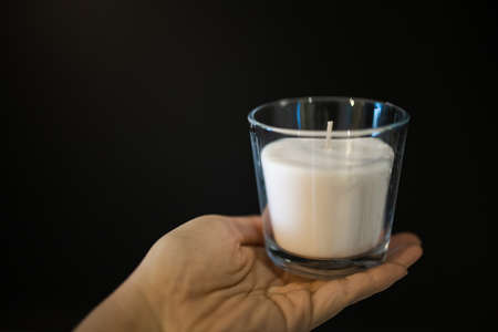 Hand holding White homemade craft candle in glass jar on black background.の写真素材