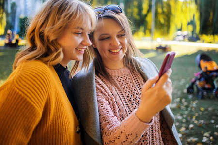 Mother with her teen daughter using phone dressed in yellow in autumn park