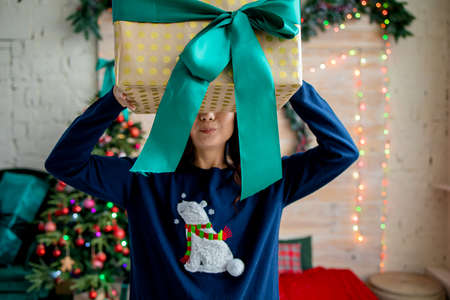 positive asian girl hold big gift box in house indoors with x-mas christmas decorationの写真素材