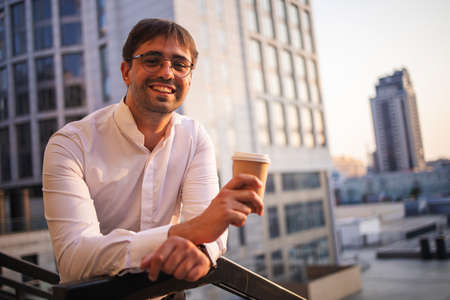 Confident young businessman using mobile phone and drinking coffee in the cityの写真素材