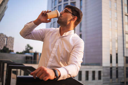 Confident young businessman using mobile phone and drinking coffee in the cityの写真素材