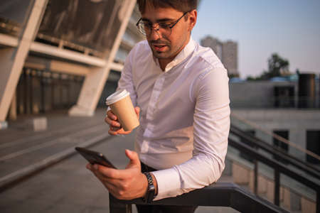 Confident young businessman using mobile phone and drinking coffee in the cityの写真素材
