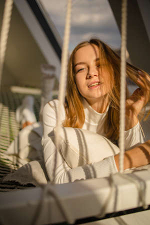 beautiful young blonde woman lies on a stretched net with sun lights on sunny day.の写真素材