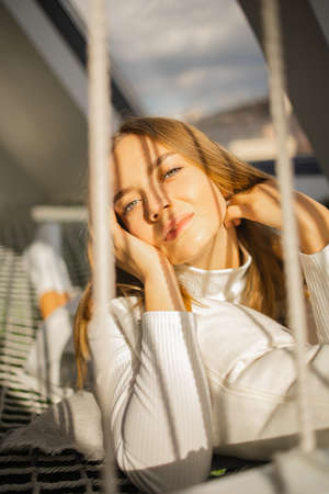 beautiful young blonde woman lies on a stretched net with sun lights on sunny day.の写真素材