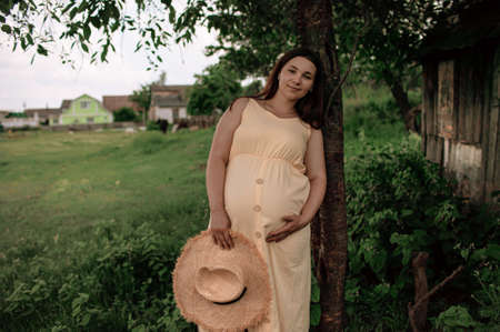 young beautiful pregnant woman walking in the green field on a sunny summer day. Nature in the...