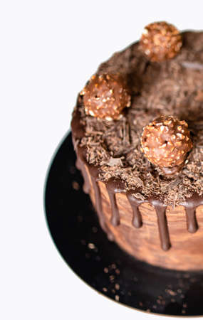 Tender chocolate cake decorated with melted dark chocolate, cake pops and candies on white table....
