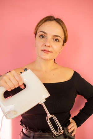 kitchen mixer in a woman's hand. Woman holds electric mixer on pink background. Clean new blender in...