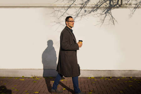 Happy Young Businessman in Casual wear with coffee cup walking by the urban building wall. Lifestyle...