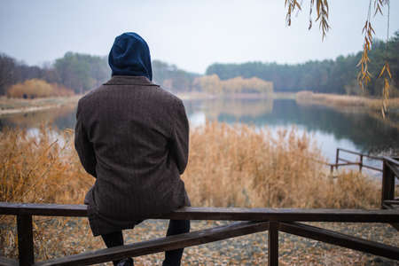A young man sits alone by the lake in cloudy foggy morning. To be alone with yourself.の写真素材