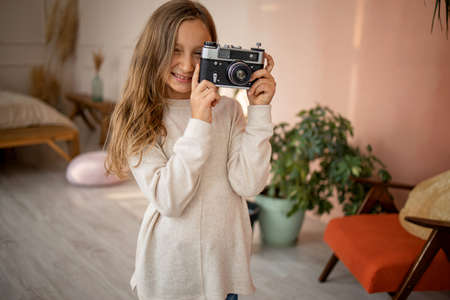 Child with a vintage camera. Portrait of a girl holding a camera in cozy home.の写真素材