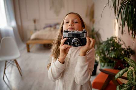 Child with a vintage camera. Portrait of a girl holding a camera in cozy home.の写真素材