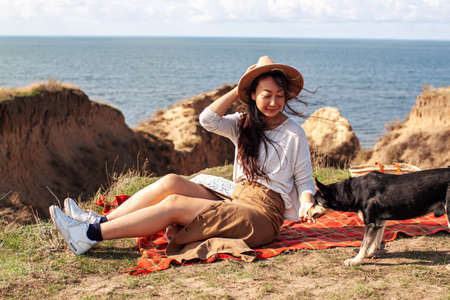 happy asian woman at sunset, relaxing with her dog on the hills.