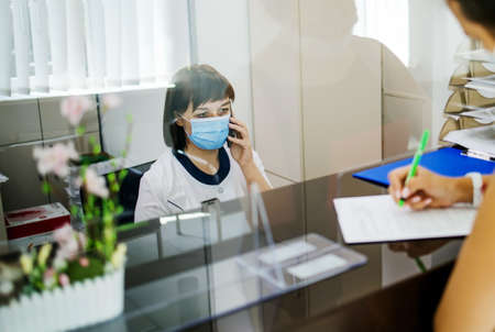 At the hospital, the nurse on duty makes a record at the reception desk. Busy modern hospital with some of the best specialists and Medicare in the country.の写真素材