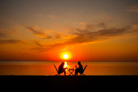 Couple drinking coffee on the beach with beautiful sunset in the backgroundの写真素材