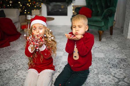 Little kids in christmas costume having fun beside a decorated christmas tree. Two kids playing with...